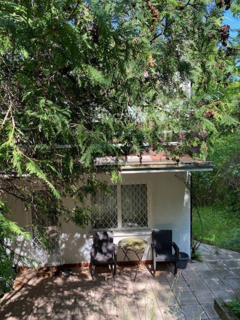 Kleine gepflasterte Terrasse mit Gartenmöbeln, umgeben von Bäumen und Sträuchern.