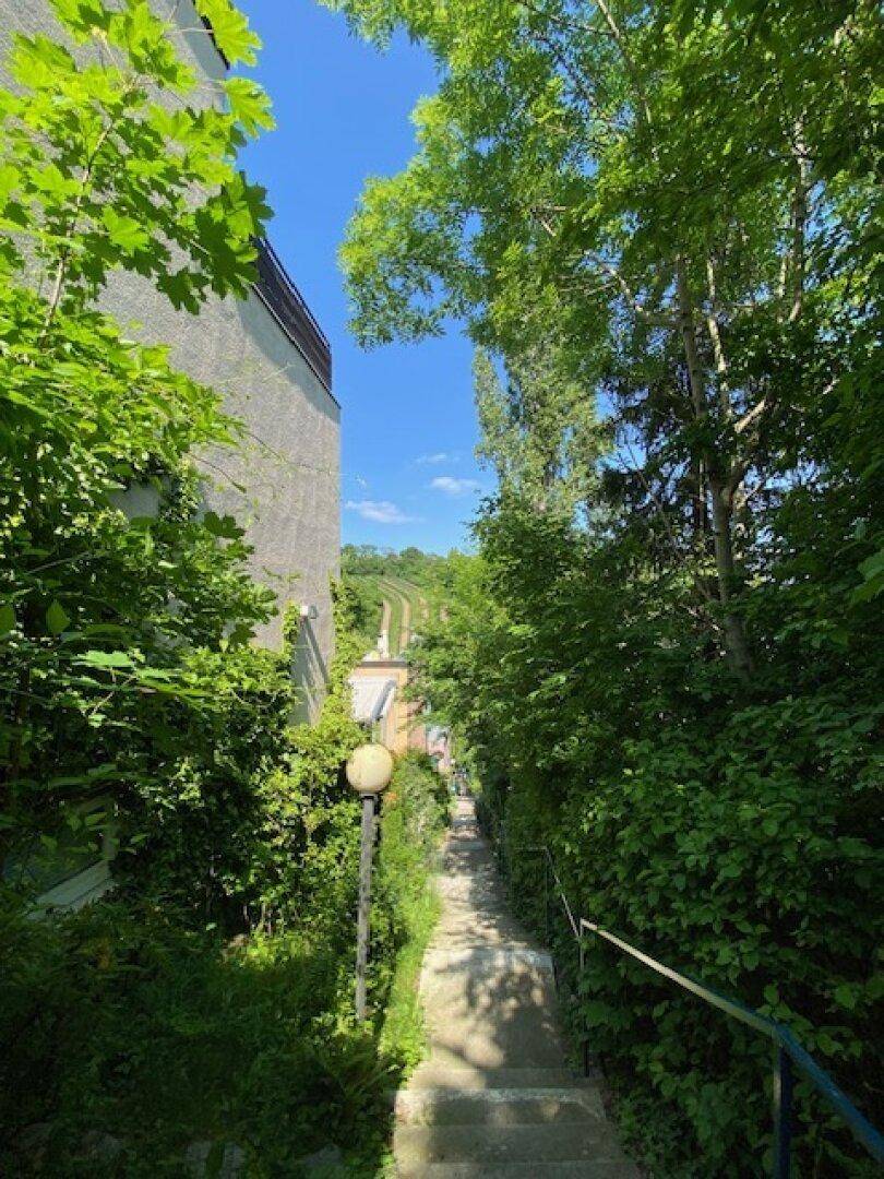 Langer, von dichtem Grün gesäumter Treppenweg führt bergauf, mit einem Gebäude auf der linken Seite.