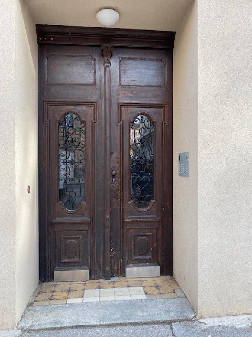 Prunkvolle, dunkle Holztür mit kunstvollen Glas- und Schmiedeeisendetails als Haupteingang des Gebäudes.