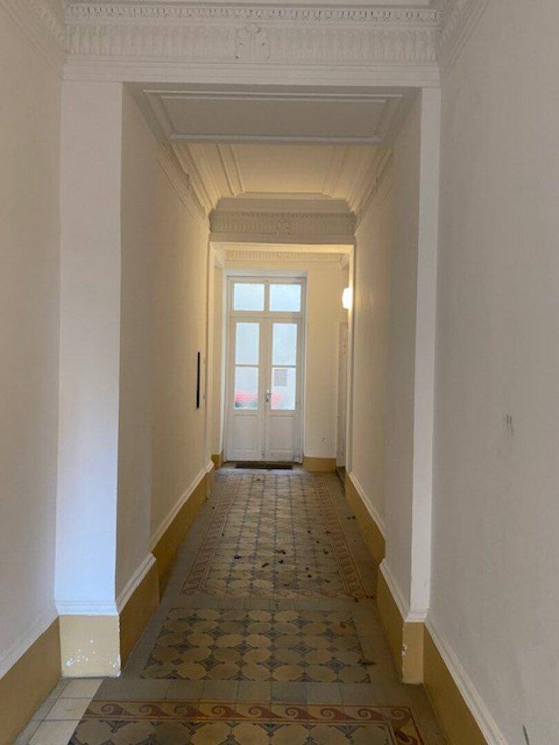 Langer Flur mit gemusterten Fliesen, hohen Decken und Stuckdetails, führt zu einem weiteren Raum.