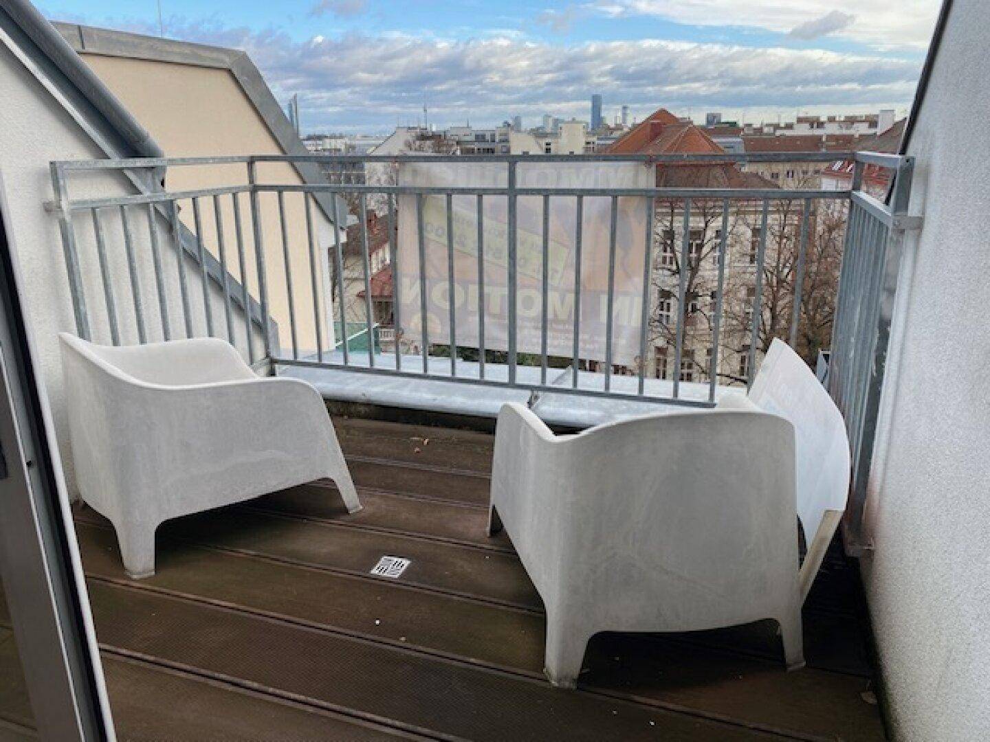 Kleiner Balkon mit zwei modernen Stühlen und Blick über die Dächer der Stadt.