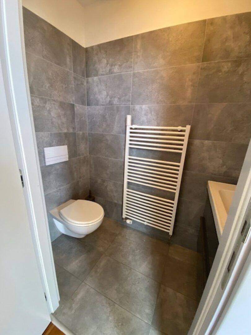 Gäste-WC mit modernen grauen Fliesen, wandhängendem WC und praktischem Handtuchheizkörper.