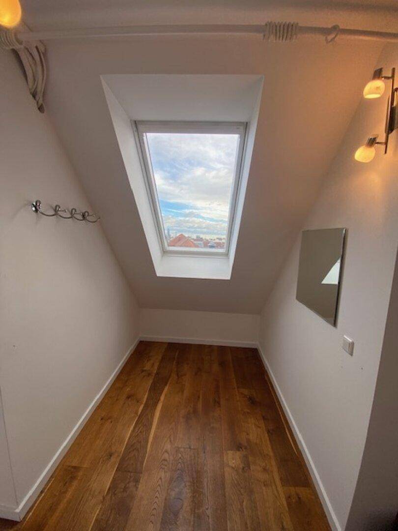Schmaler Flur mit Holzboden, Dachschräge und einem einzelnen Dachfenster für natürliches Licht.