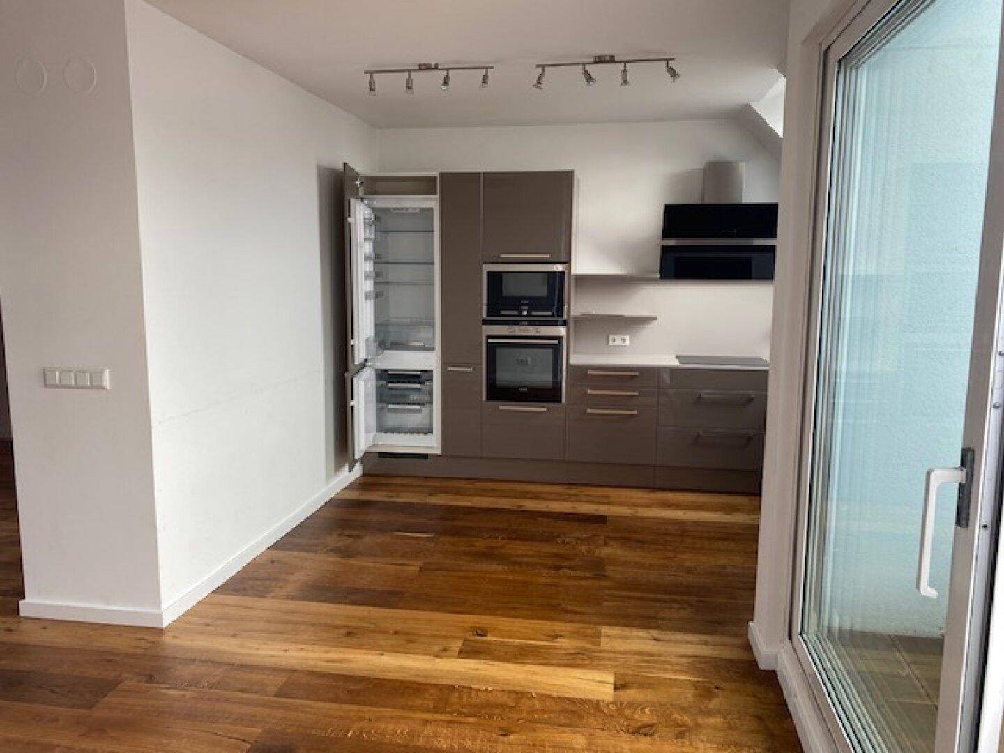 Geräumige Küche mit modernen Einbauschränken, integriertem Kühlschrank und Holzboden.