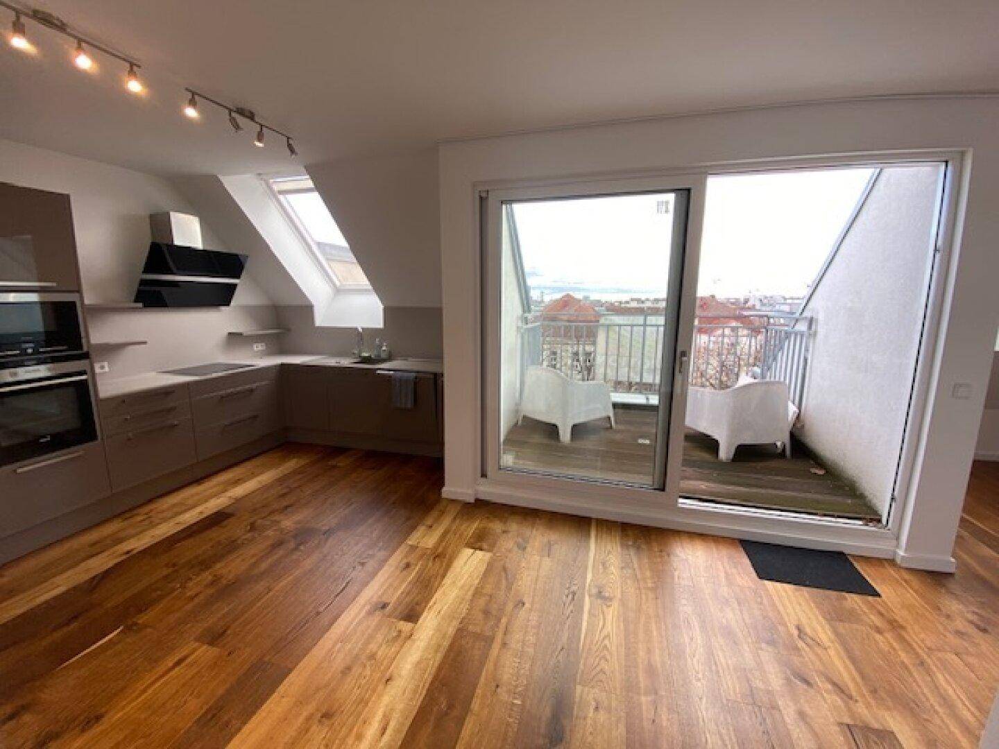 Offene Küche mit Holzboden und Zugang zu einem kleinen Balkon mit Sitzgelegenheiten.