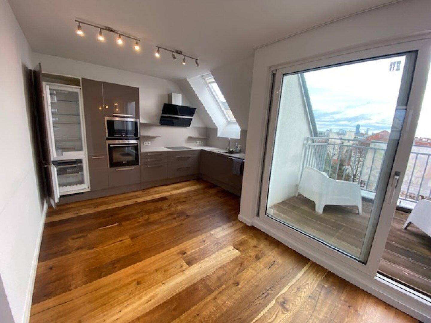 Offene Wohnküche mit Holzboden und Schiebetür zum Balkon, ideal für Mahlzeiten im Freien.