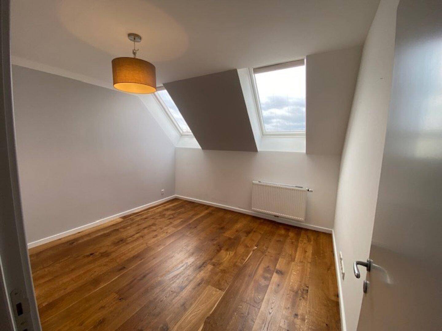 Gemütliches Schlafzimmer mit Holzboden, Dachschräge, Dachfenster und Heizkörper.