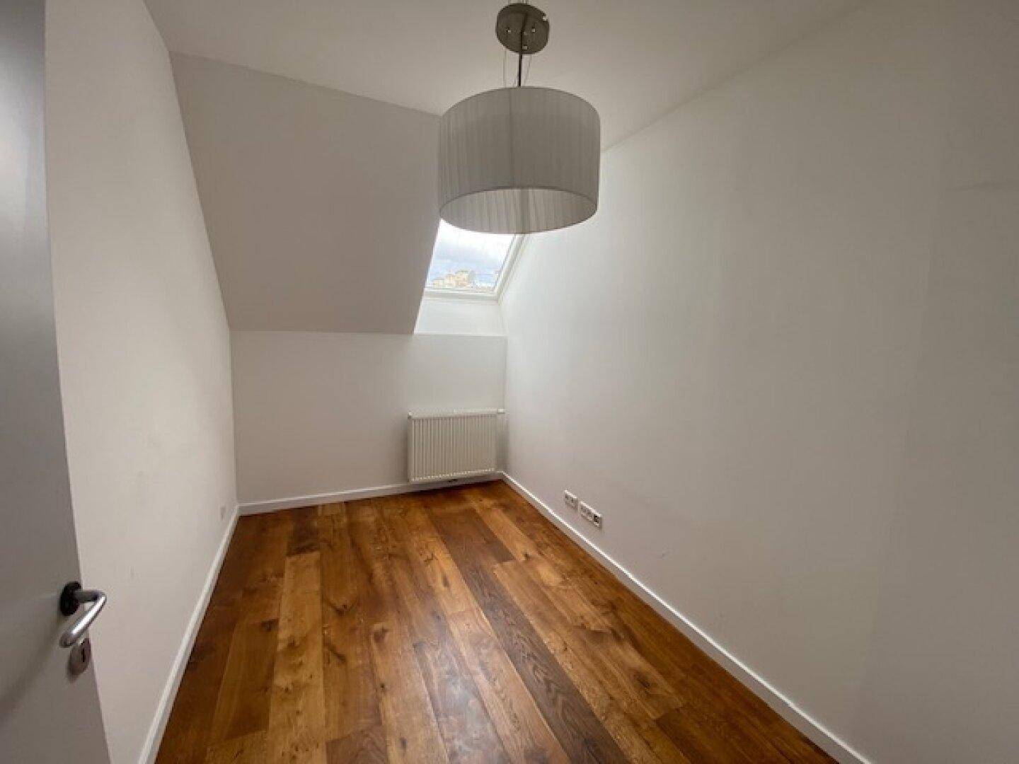 Helles Zimmer mit Holzboden, Dachschräge und einem Dachfenster, ideal als Kinder- oder Arbeitszimmer.