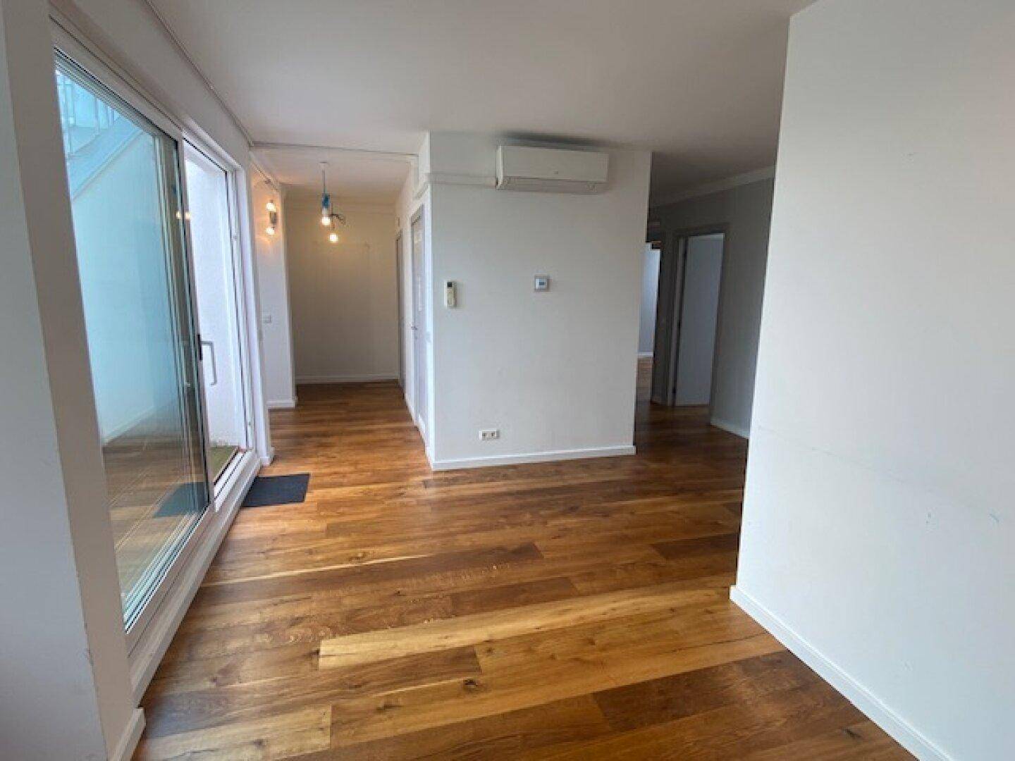 Heller Eingangsbereich mit Holzboden, Klimaanlage und großem Fenster mit Zugang nach draußen.