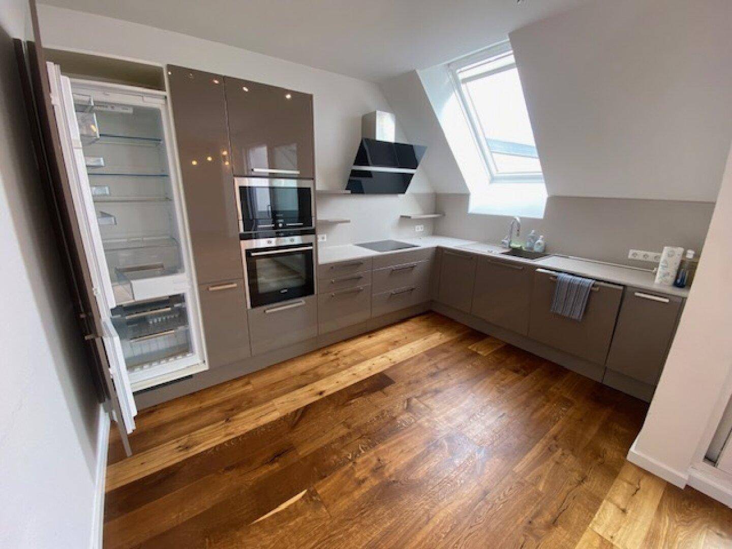 Moderne Einbauküche mit braunen Schränken, integrierten Geräten und Holzboden im Dachgeschoss.