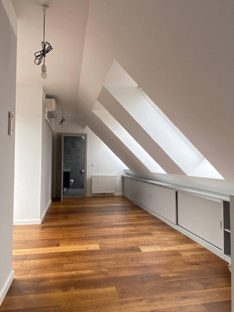 Heller Raum mit Holzboden, Dachschräge, integrierten Schränken und Klimaanlage.