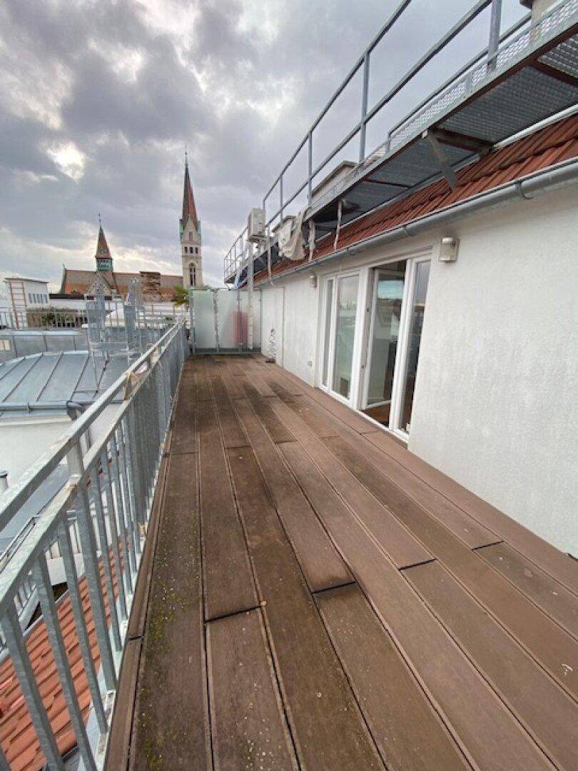Weitläufige Dachterrasse mit Holzboden und Metallgeländer, bietet Blick auf die Stadt und Kirchtürme.