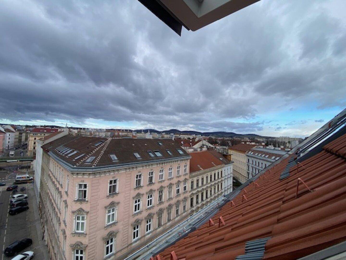Blick von oben auf eine belebte Stadtstraße mit historischen Gebäuden und roten Ziegeldächern.