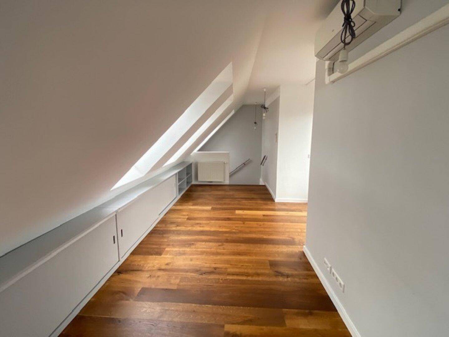 Geräumiger Dachgeschossraum mit Holzboden, praktischen Einbauschränken und viel Tageslicht.