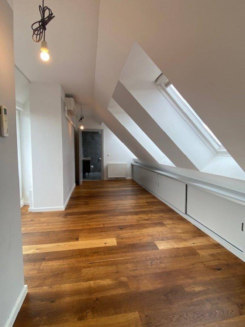 Heller Dachgeschossraum mit Holzboden, Einbauschränken und Zugang zu einem angrenzenden Badezimmer.