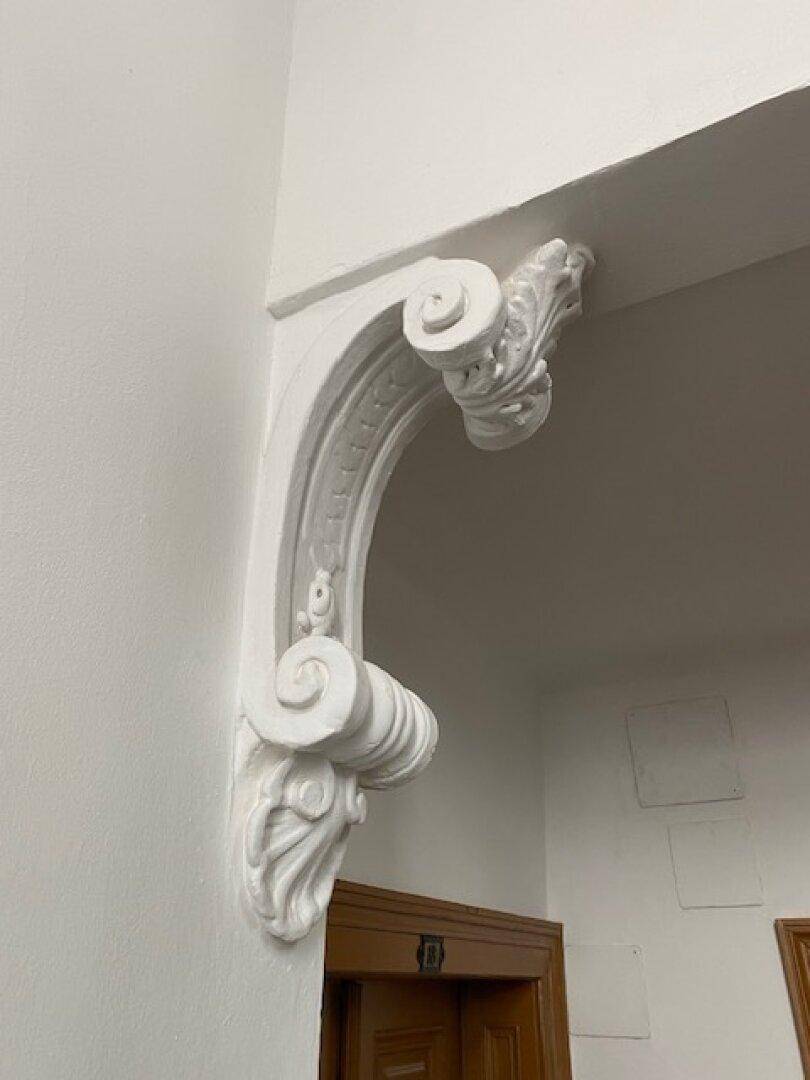Detailansicht eines weißen, kunstvollen Stuckelements an der Wand, das architektonische Eleganz verleiht.
