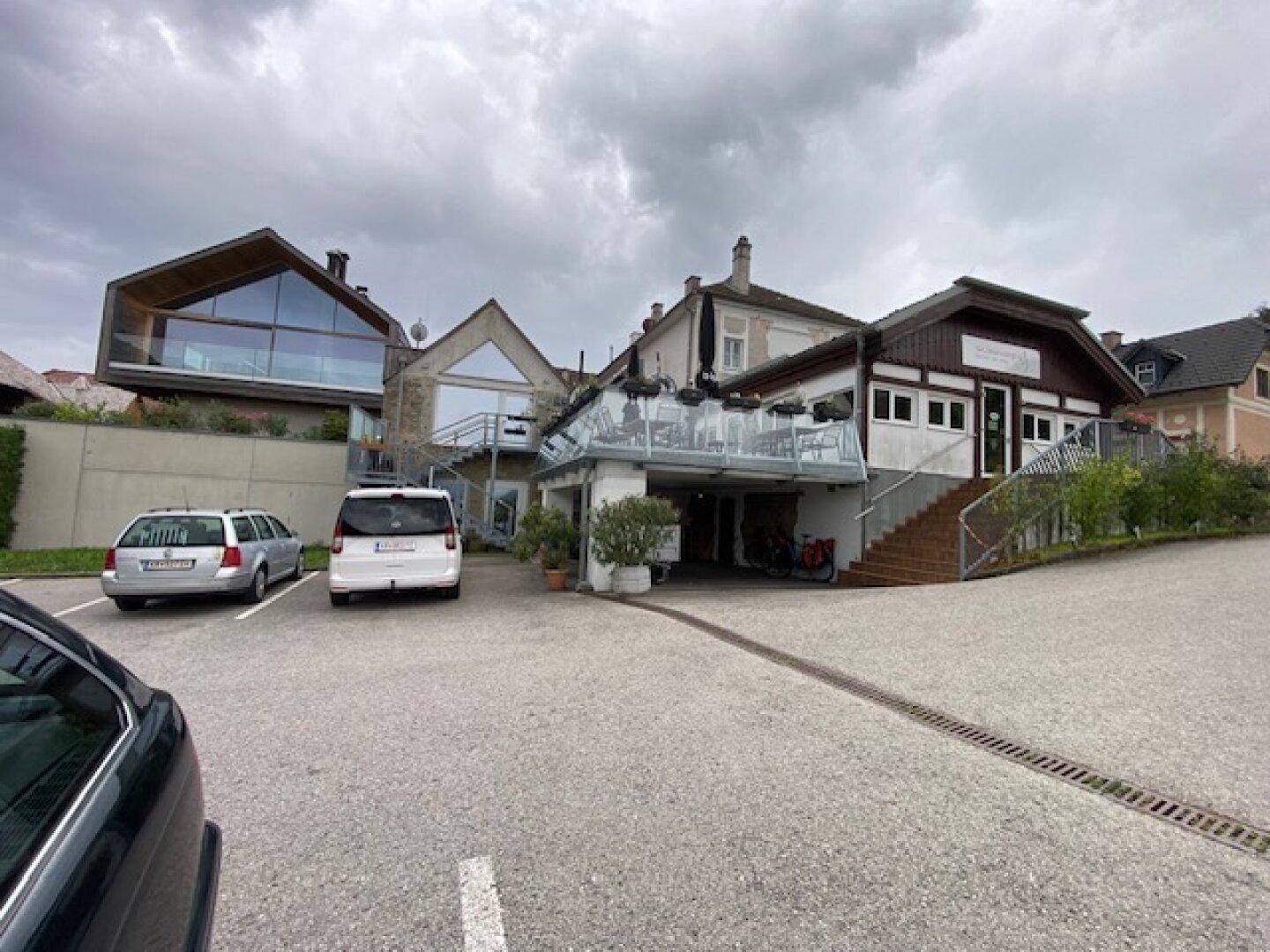 Außenansicht eines Gebäudekomplexes mit moderner Glasfassade und traditionellen Elementen sowie einem Parkplatz.