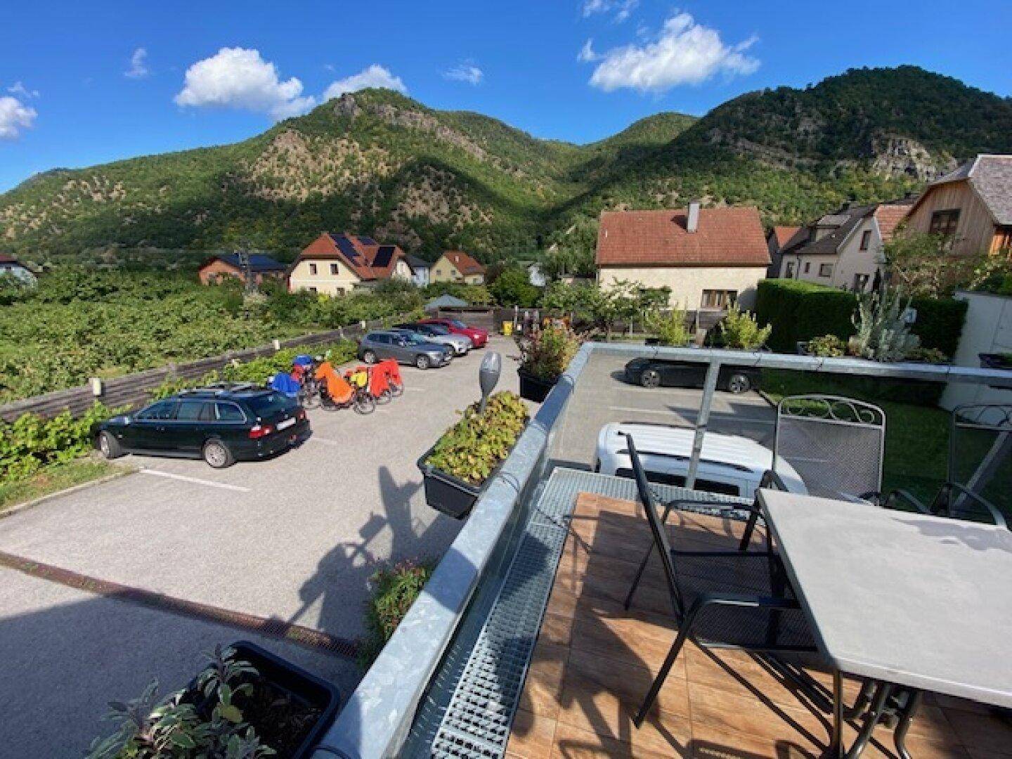 Sonniger Terrassenbereich mit Blick auf einen Parkplatz und die umliegende Berglandschaft.