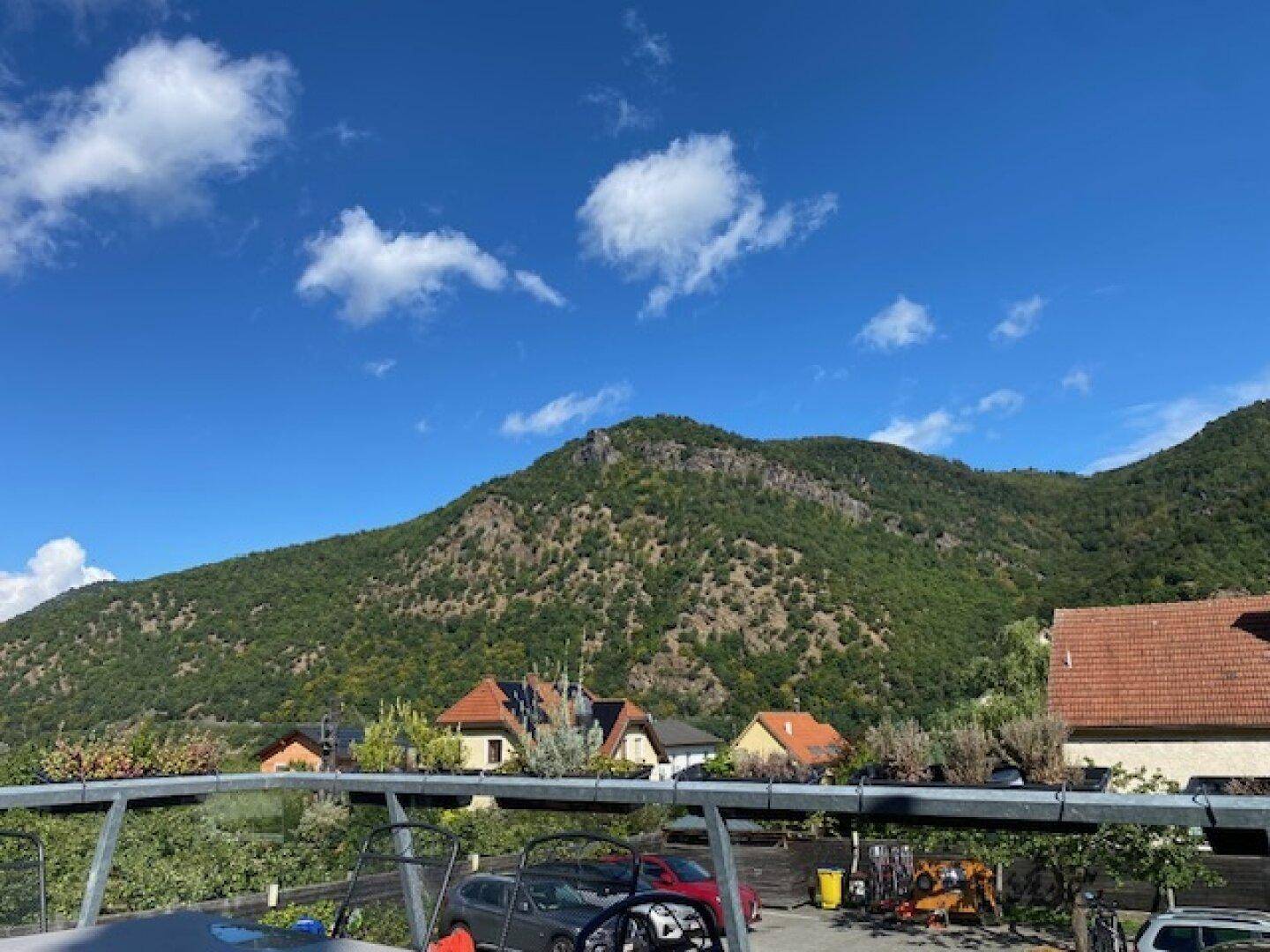 Panoramablick auf einen bewaldeten Berg mit Häusern am Fuße unter einem strahlend blauen Himmel.