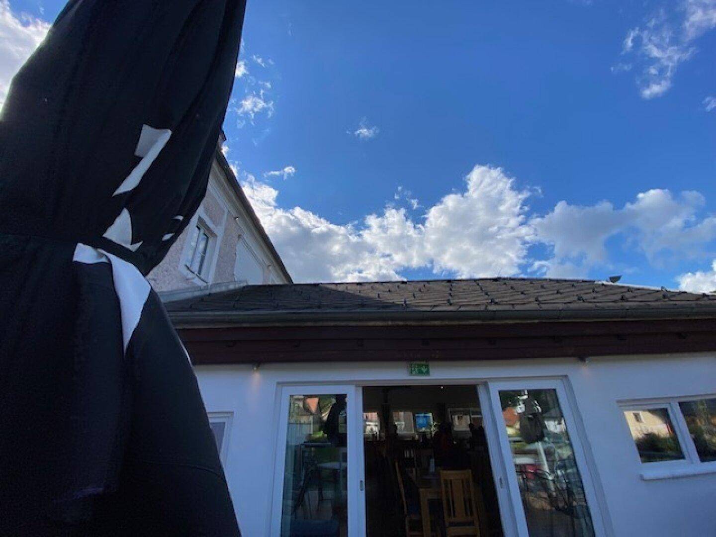 Außenansicht eines Gebäudes mit dunklem Dach und weißen Wänden unter einem klaren blauen Himmel.