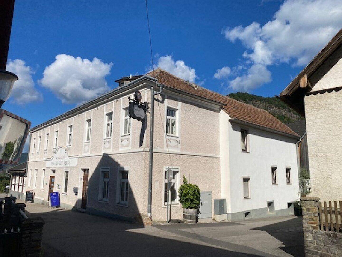 Historisches Gebäude mit heller Fassade und traditionellem Satteldach in ländlicher Umgebung.