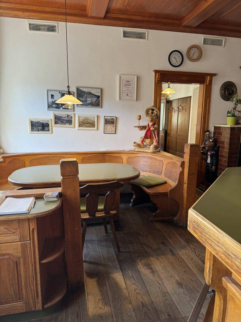 Rustikaler Essbereich mit Holzbänken, Tischen und traditioneller Dekoration, darunter Uhren und Bilder.