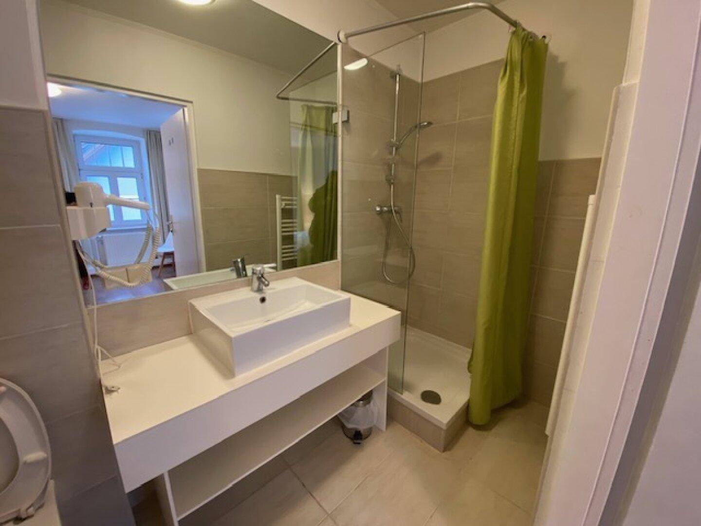 Helles Badezimmer mit modernem Waschbecken, Spiegel und Duschkabine mit Vorhang.