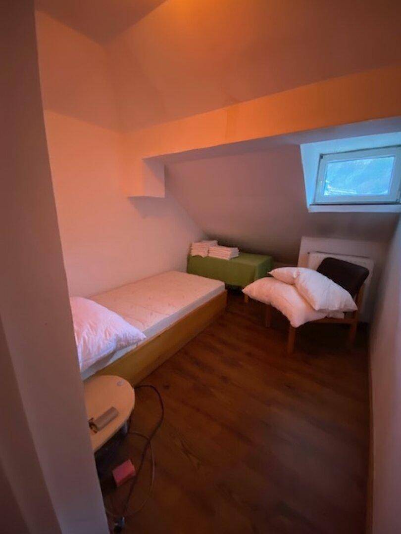 Kleines Schlafzimmer unter dem Dach mit Einzelbett, Holzboden und Dachfenster für natürliches Licht.