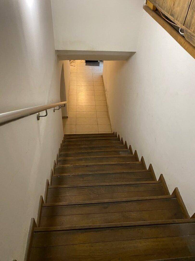 Holztreppe führt hinunter zu einem gefliesten Bereich, der einen Flur oder Keller andeutet.