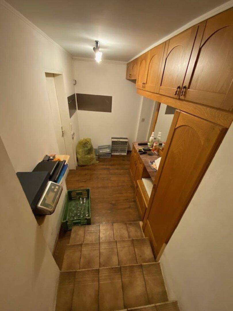 Flur oder Hauswirtschaftsraum mit Treppe, Holzschränken und verschiedenen gelagerten Gegenständen.