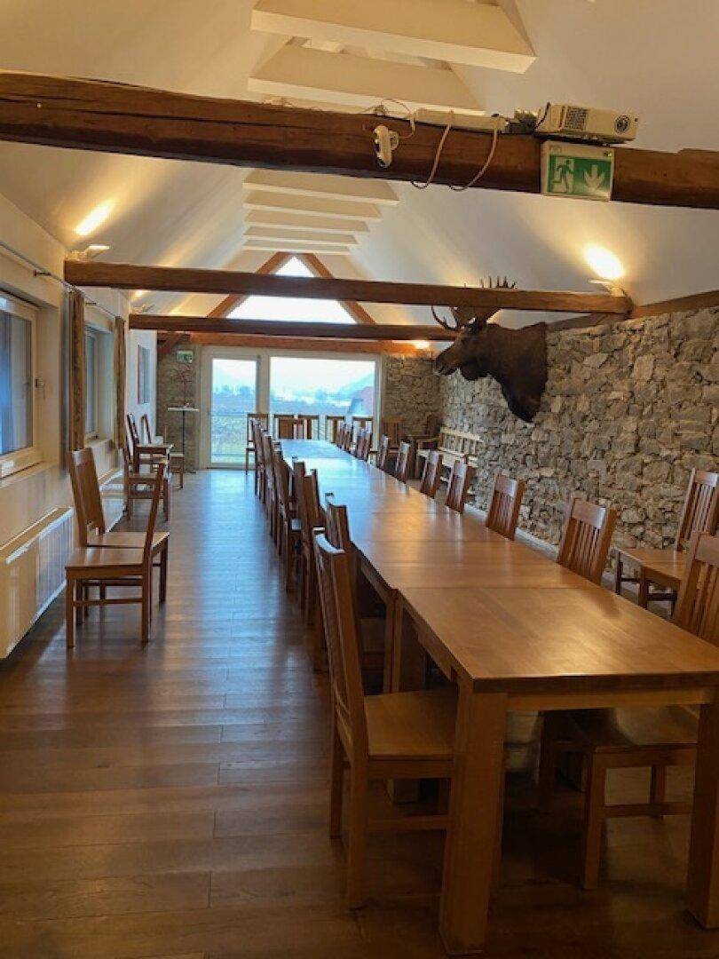 Weiterer Blick in den großen Speisesaal mit langer Tafel, Steinwand und traditioneller Hirschgeweih-Dekoration.
