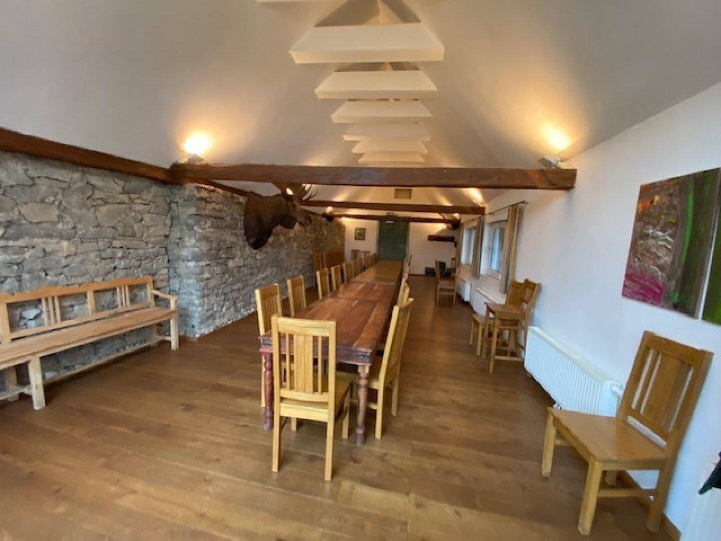 Großer Speisesaal mit langem Holztisch, Steinwand, sichtbaren Holzbalken und Hirschgeweih-Dekoration.