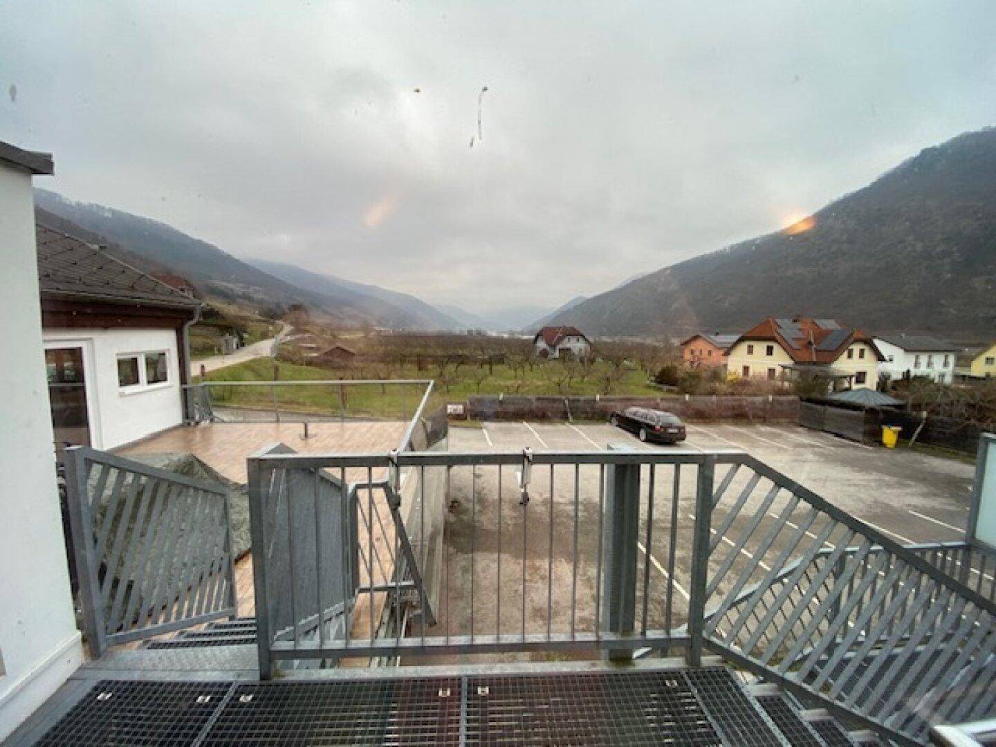 Großer Parkplatz mit Blick auf eine weite Tal- und Berglandschaft unter bewölktem Himmel.