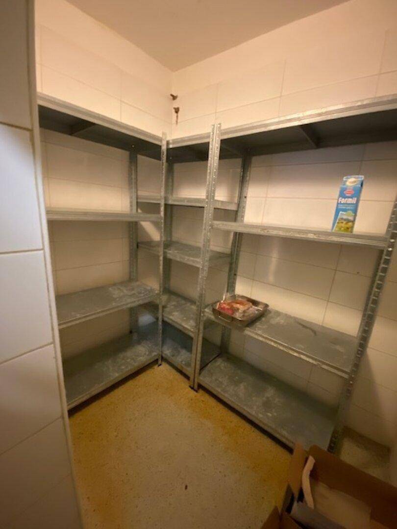 Lagerraum mit Metallregalen und gefliesten Wänden für die Aufbewahrung von Vorräten.