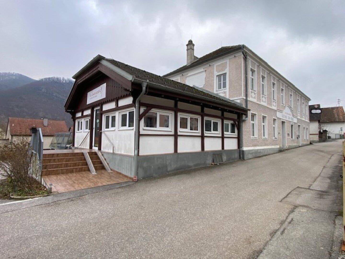 Traditionelles Gebäude mit weißer Fassade und dunklen Holzelementen an einer Straße unter bewölktem Himmel.