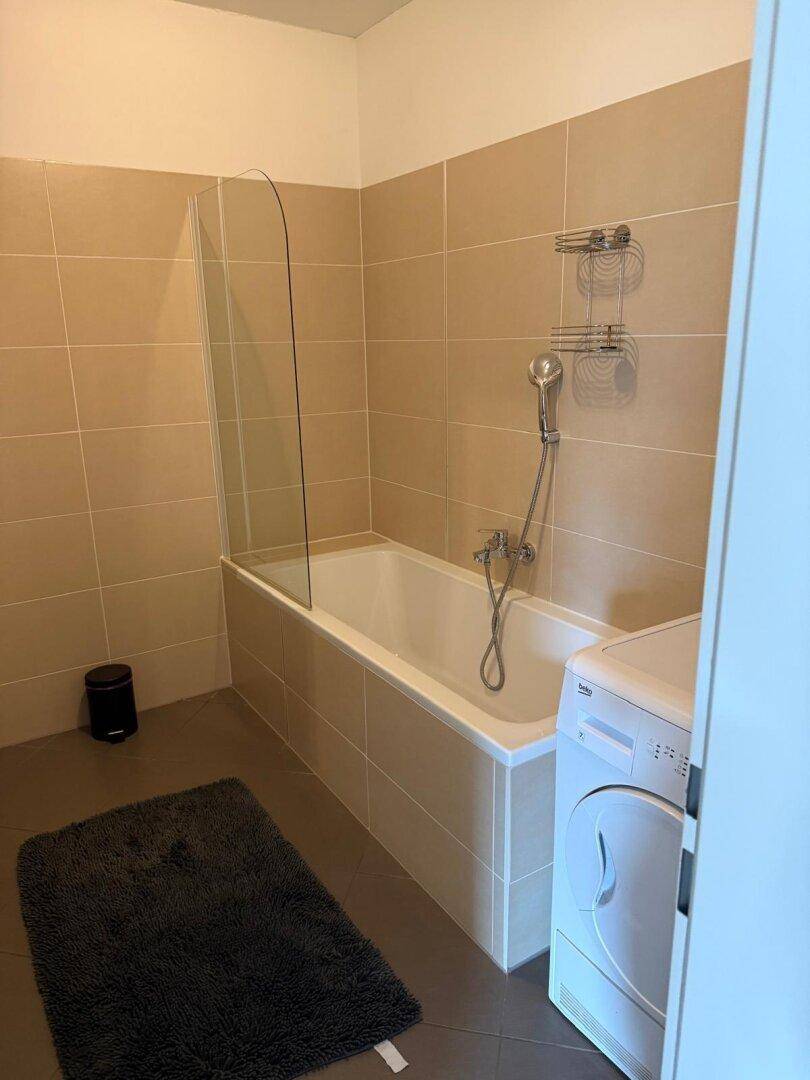 Badezimmer mit Badewanne, Duschabtrennung und beigefarbenen Fliesen.
