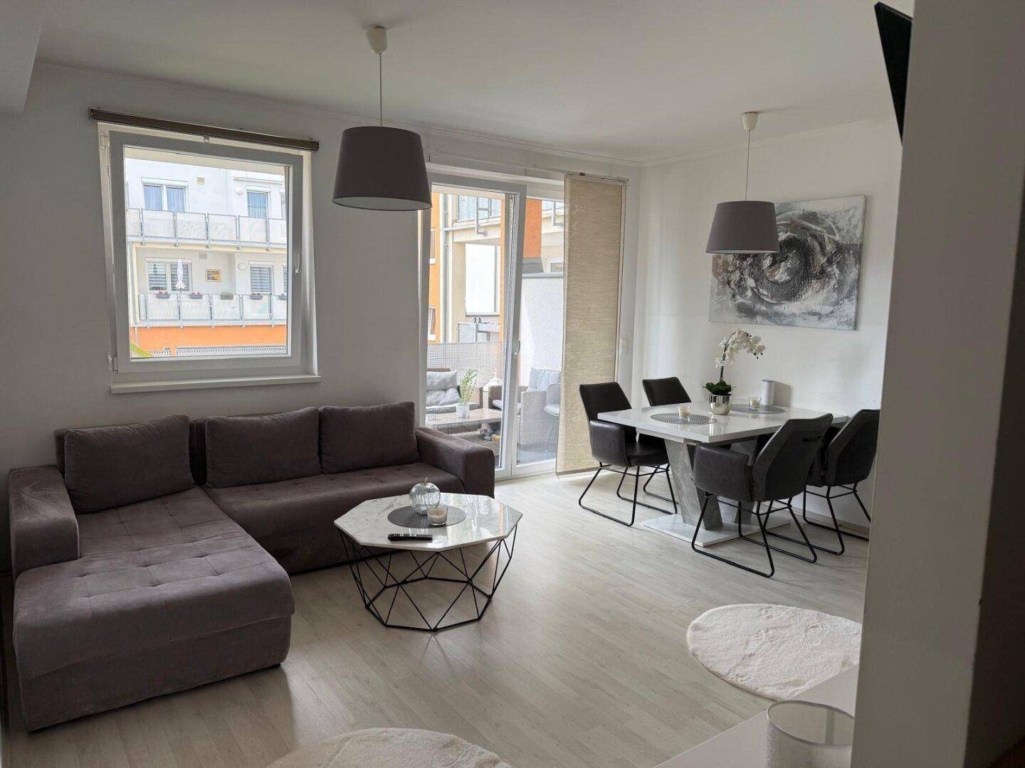 Heller Wohn-Essbereich mit modernem Sofa, Esstisch und Zugang zum Balkon.