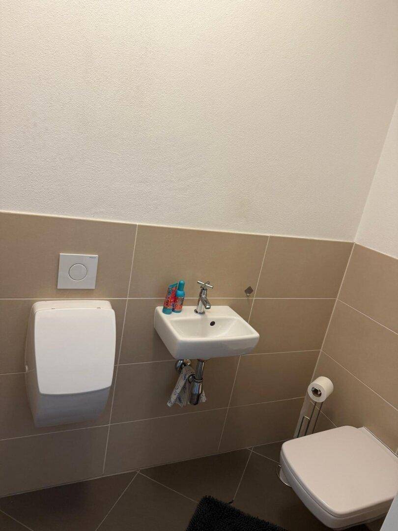 Kleines Gäste-WC mit Waschbecken und Wand-WC in beigefarbenen Fliesen.