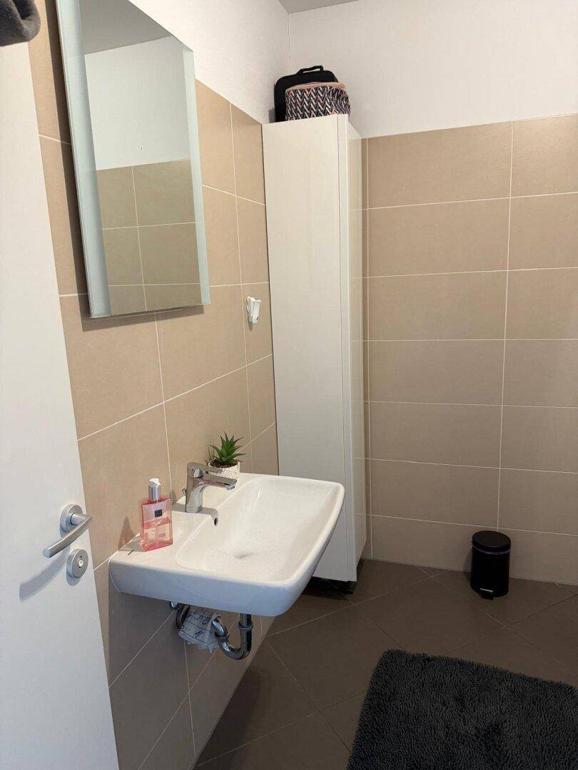Badezimmer mit modernem Waschbecken, Spiegel und beigefarbenen Fliesen.
