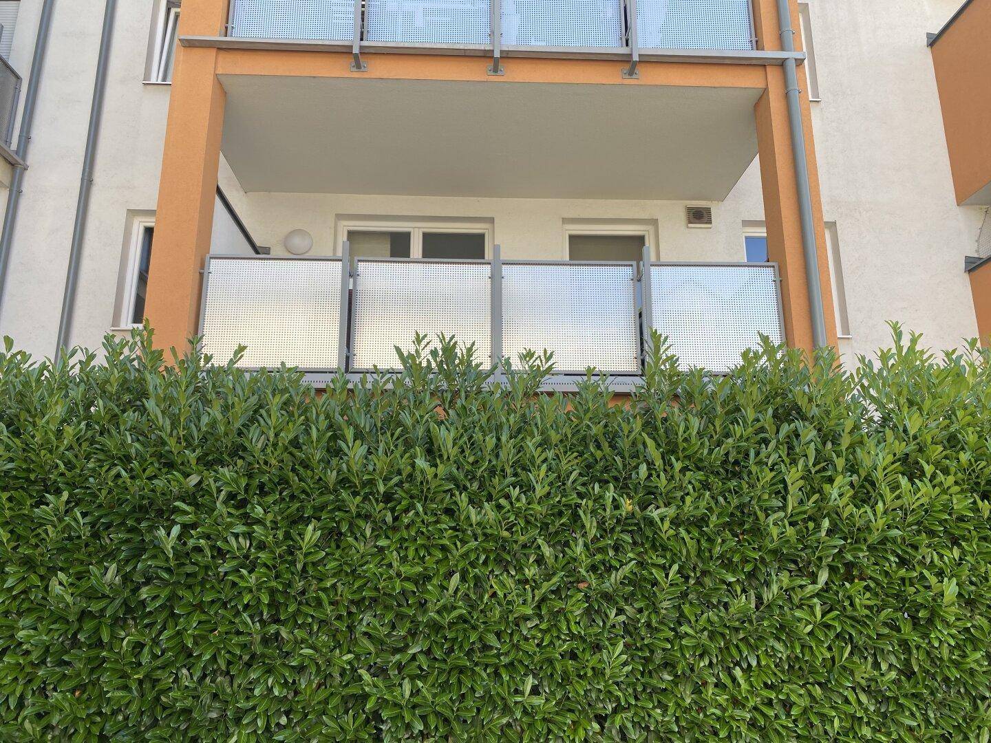 Balkon mit moderner Glasbrüstung und Blick auf die grüne Hecke.