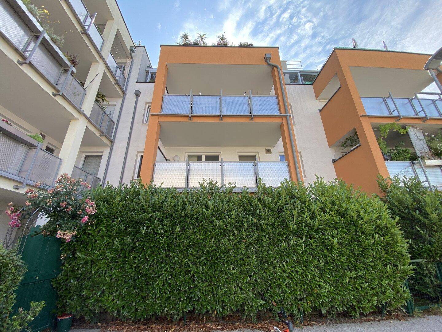 Moderne Wohnanlage mit Balkonen und gepflegter Hecke im Vordergrund.