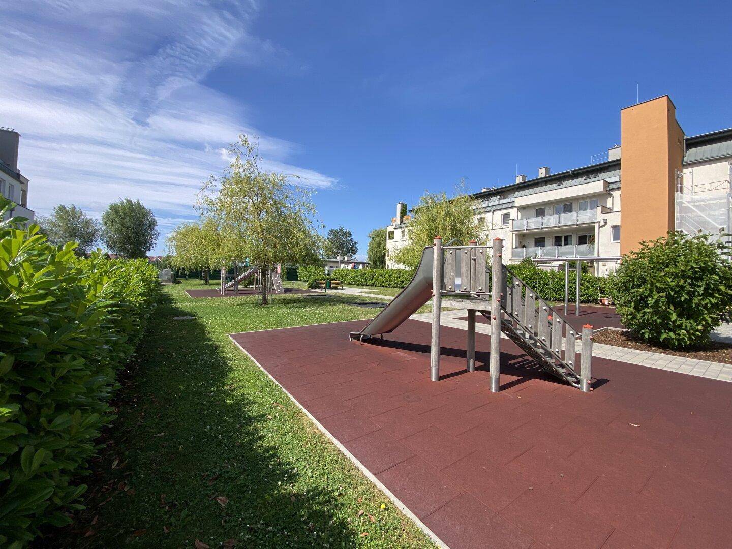 Kinderspielplatz mit Rutsche und Fallschutzboden in einer grünen Umgebung.