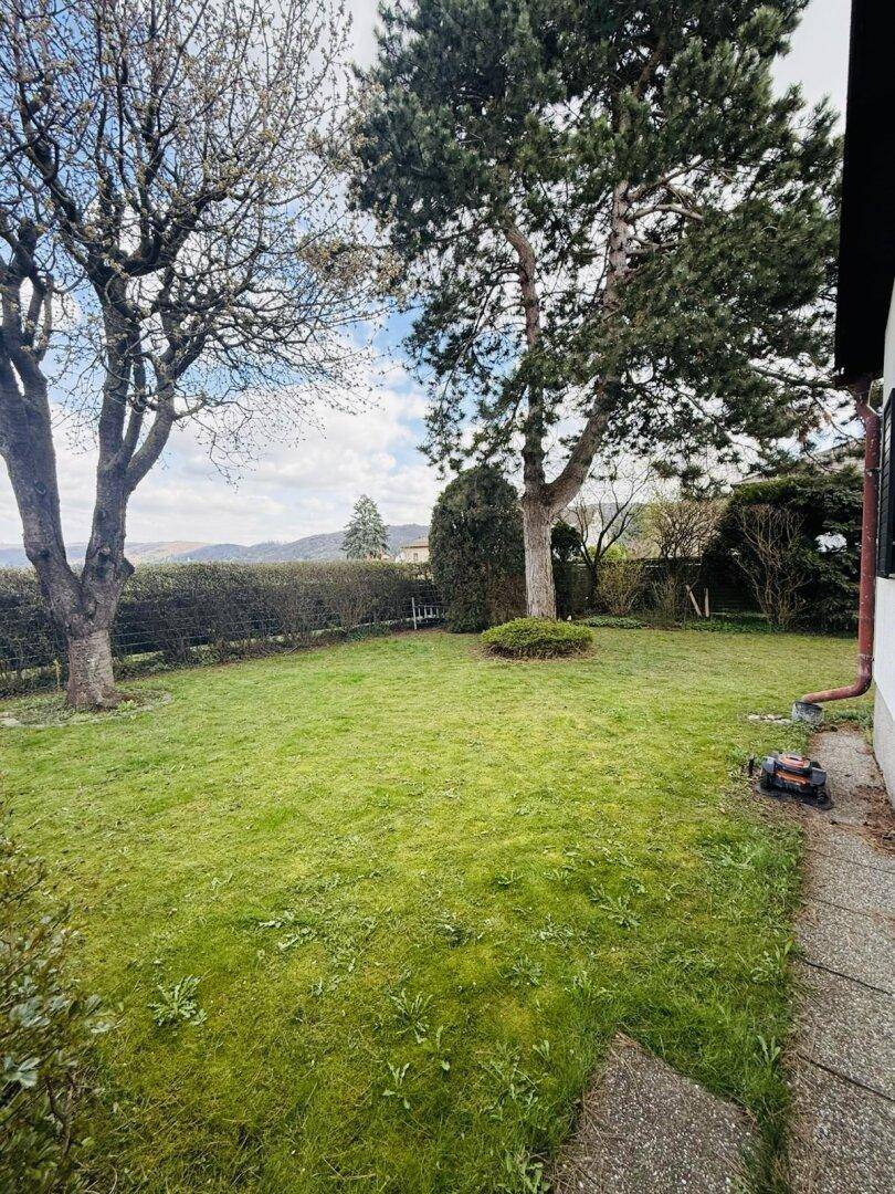 Sonniger Garten mit Rasenfläche, Bäumen und einem weiten Blick in die umliegende Landschaft.