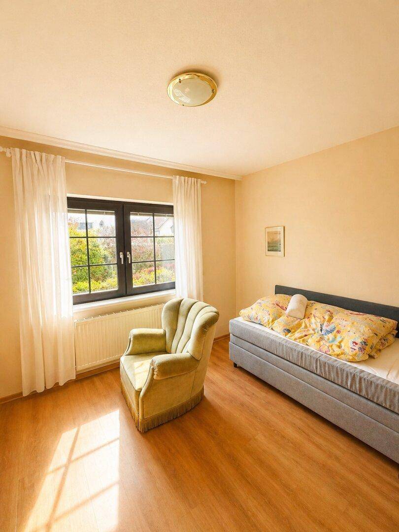 Helles Schlafzimmer mit Holzboden, einem Einzelbett und einem gemütlichen Sessel am Fenster.