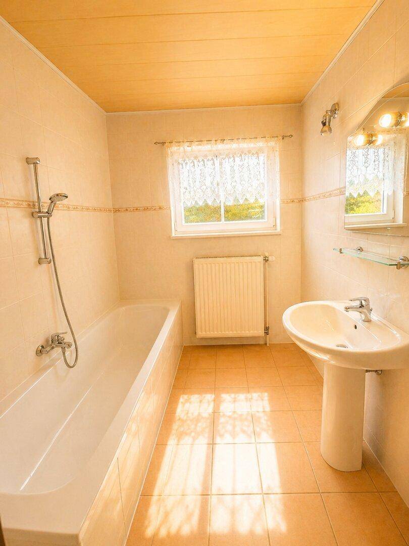 Badezimmer mit Badewanne, Duschvorrichtung, Waschbecken und einem Fenster für natürliches Licht.