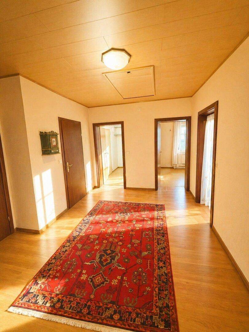 Heller Flur mit Holzboden, einem traditionellen Teppich und mehreren Türen zu angrenzenden Räumen.