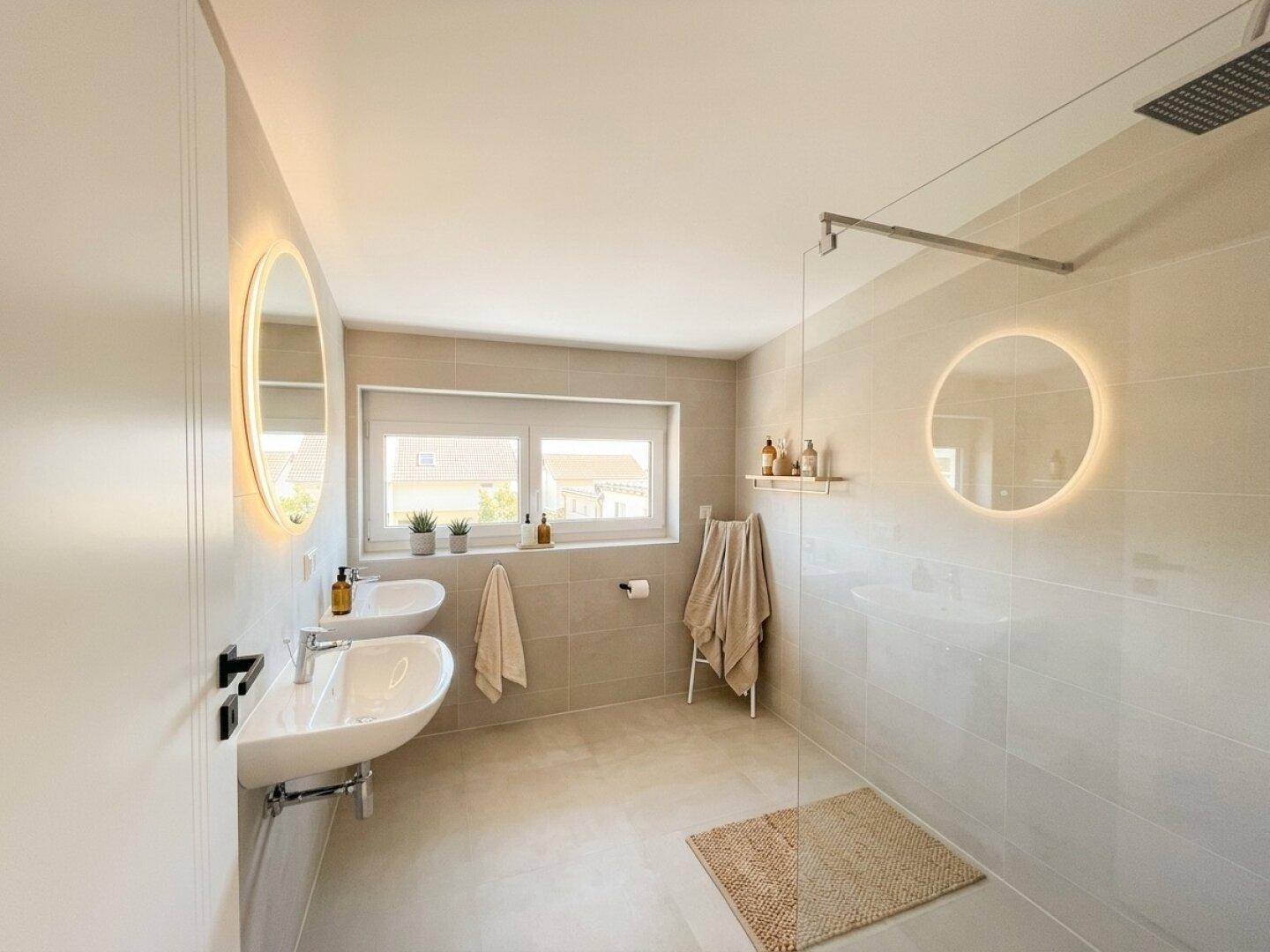 Modernes Badezimmer mit Doppelwaschbecken, großer Dusche und beleuchteten Spiegeln.