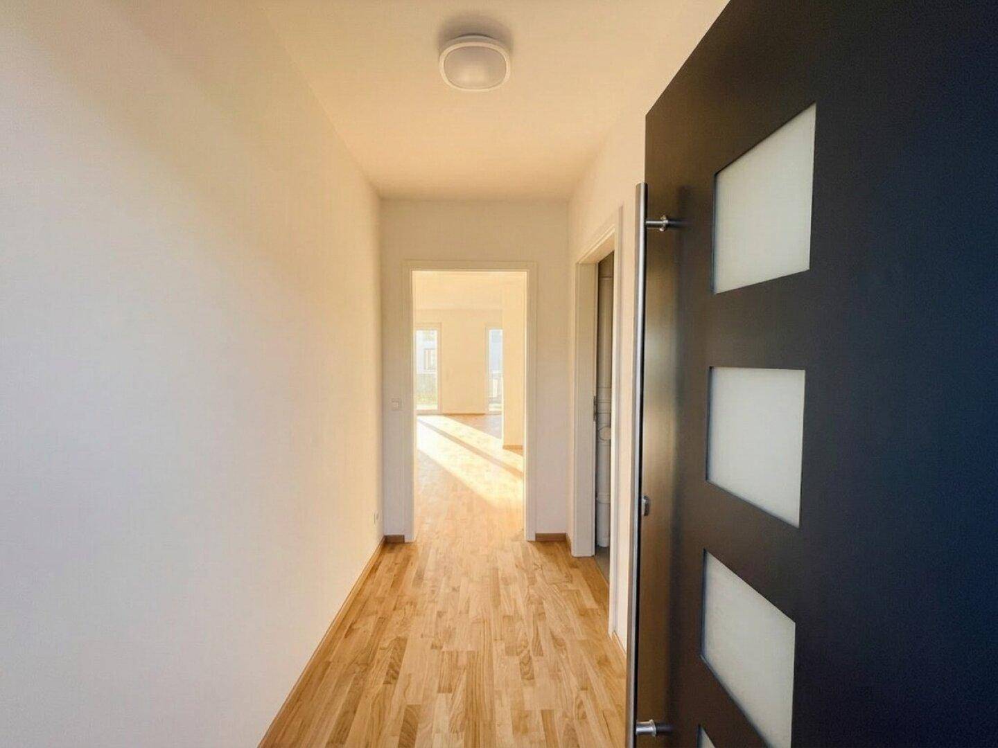 Heller Flur mit Holzboden und moderner Eingangstür, der zu weiteren Räumen führt.