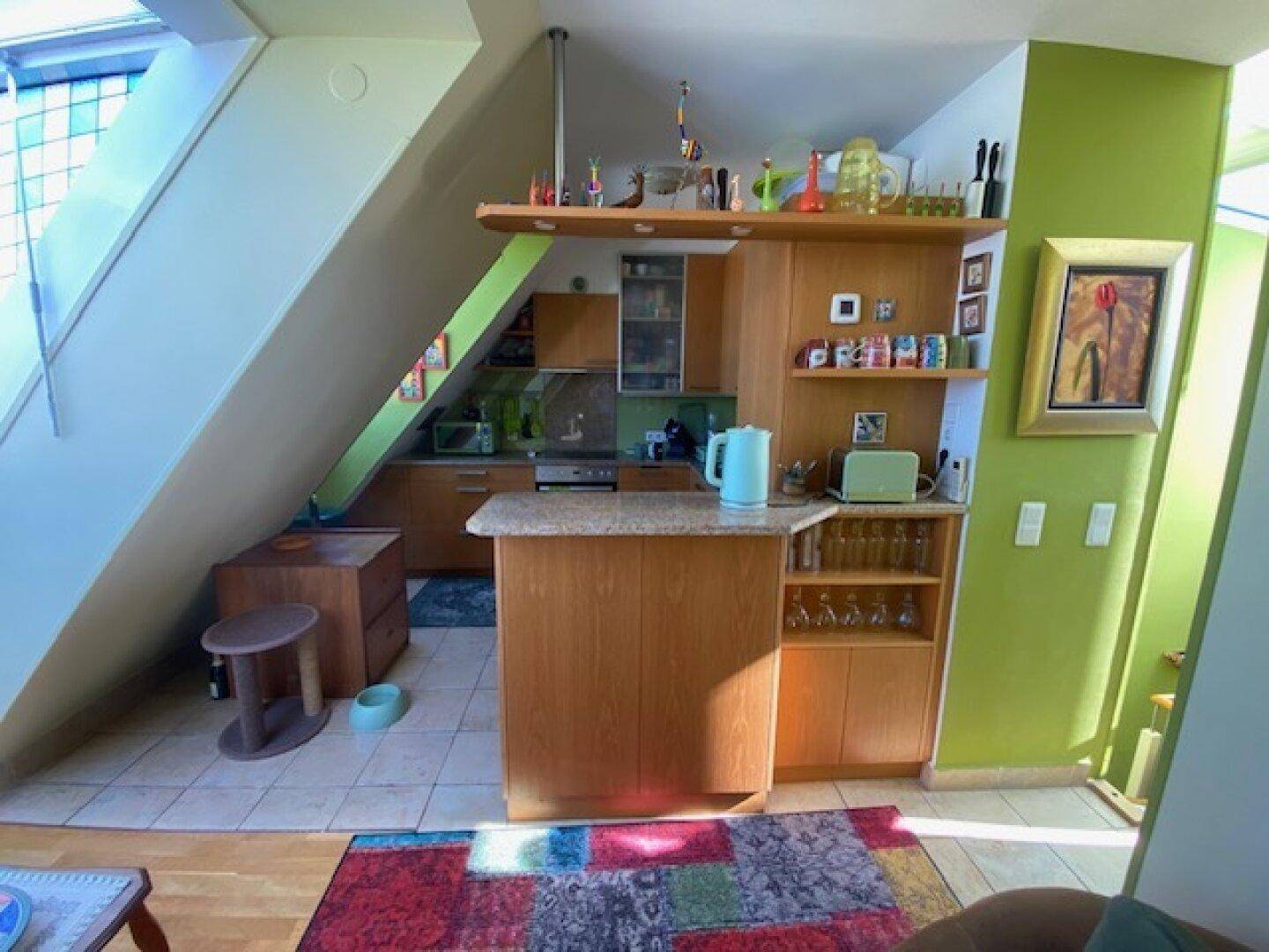 Offene Küche mit Frühstücksbar und Holzmöbeln, integriert in den Wohnbereich unter der Dachschräge.