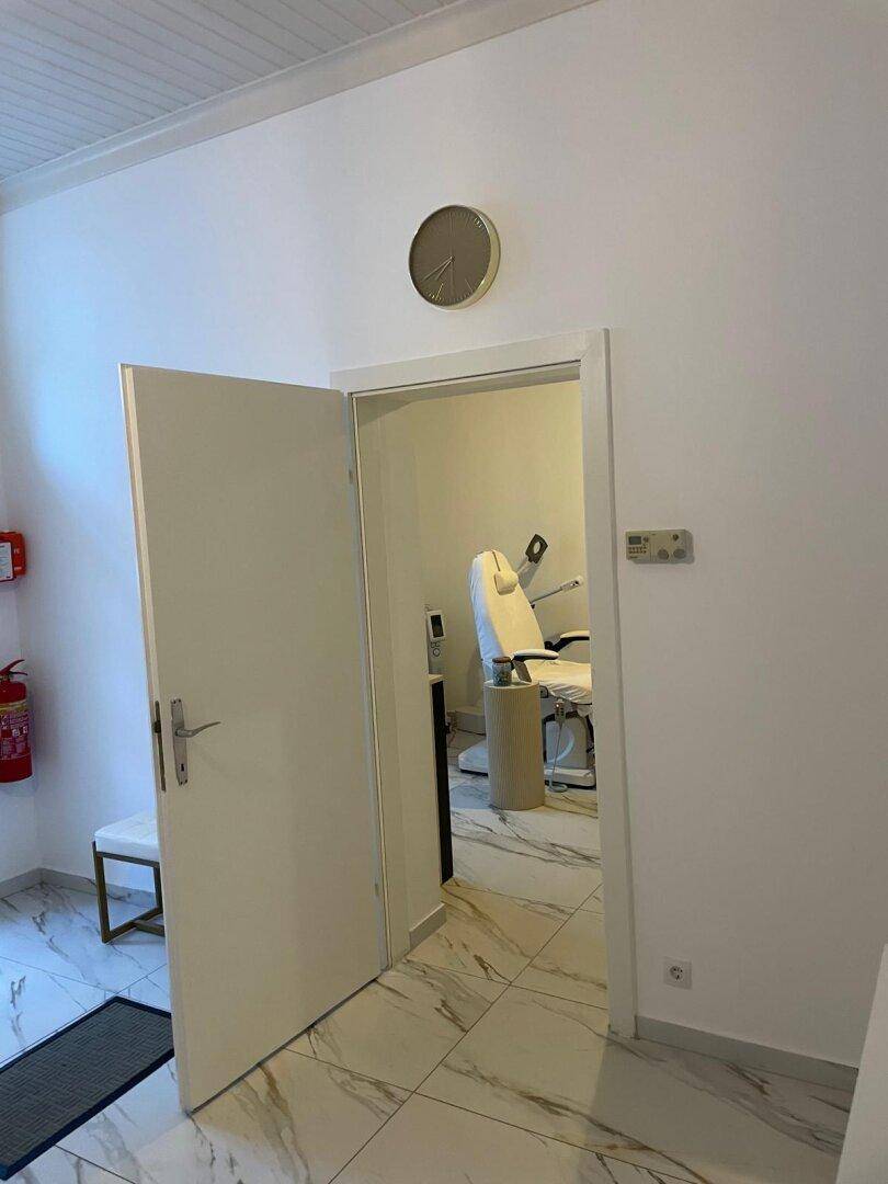 Blick durch eine offene Tür in einen Behandlungsraum mit einem weißen Behandlungsstuhl.